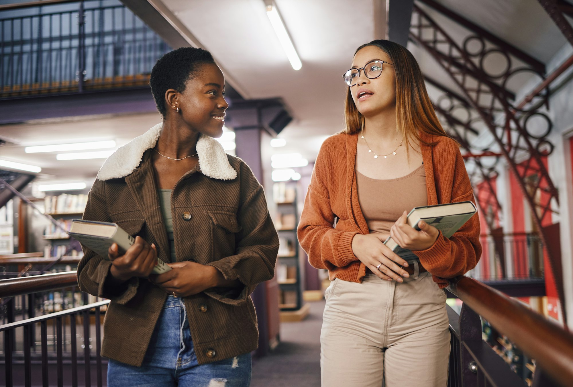 College students, library books and women talking about education and learning together at univers