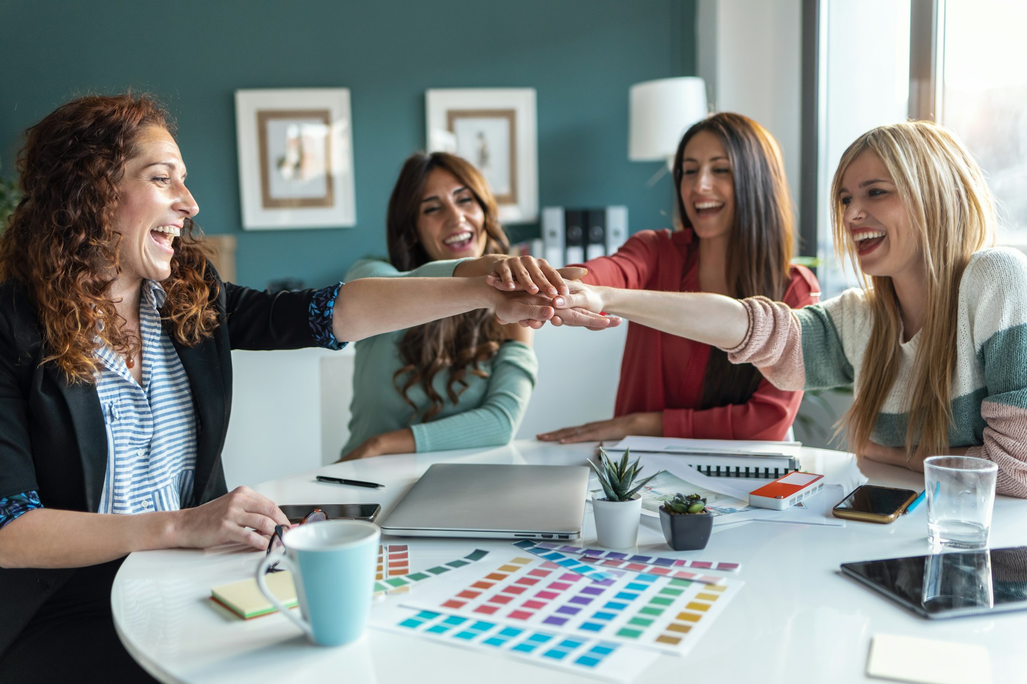 Group of successful multiage designer women celebrating good job while holding up their right hands.